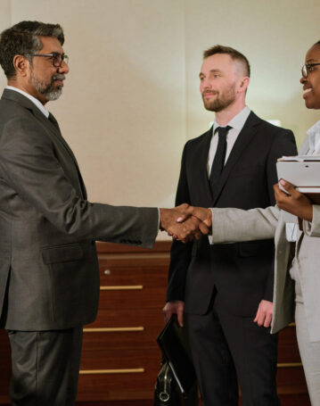 Businesswoman shaking hand of partner Happy young African American businesswoman with folder and notebook shaking hand of confident mature male director of company